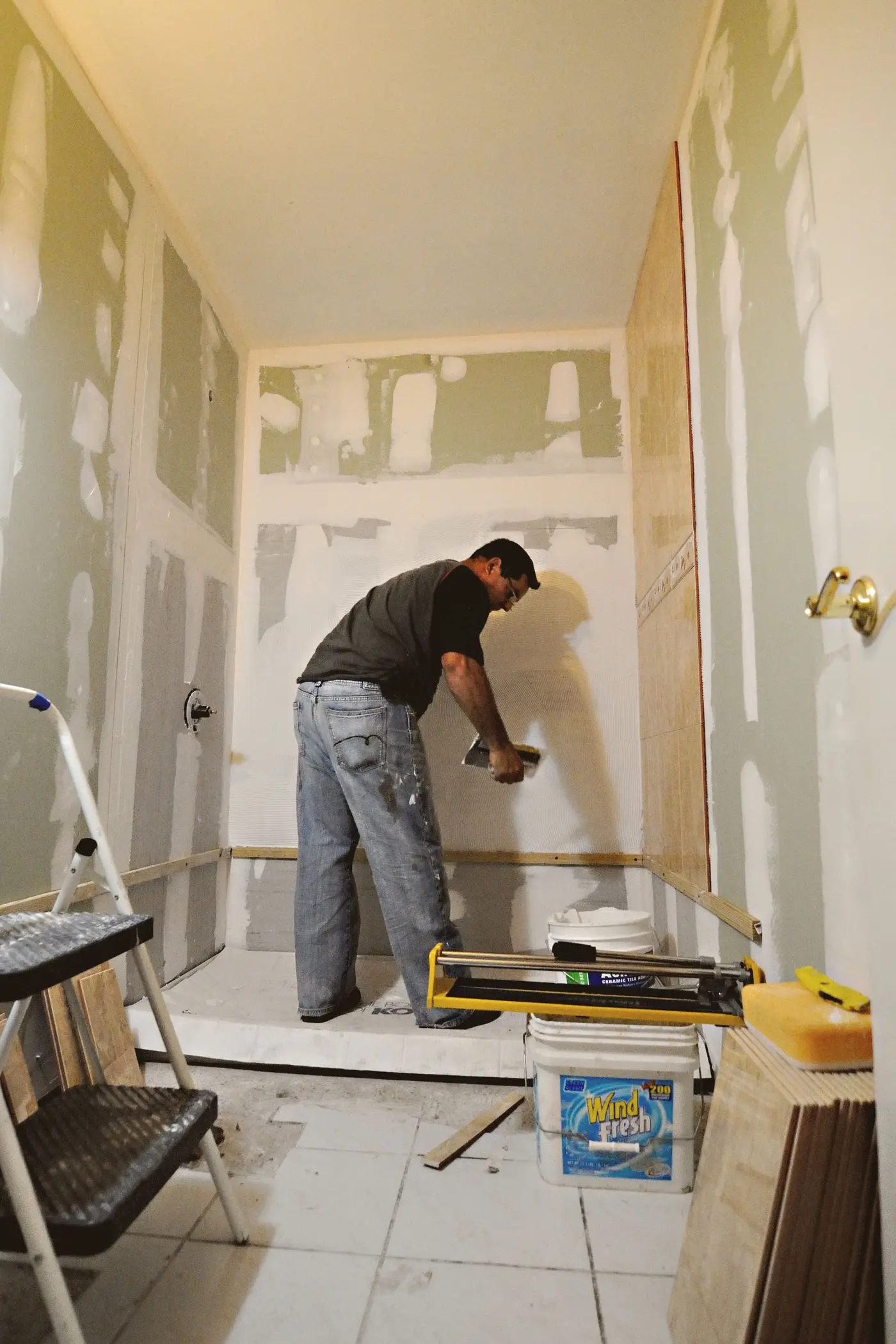 Worker spreading adhesive to tile a shower wall during a bathroom renovation