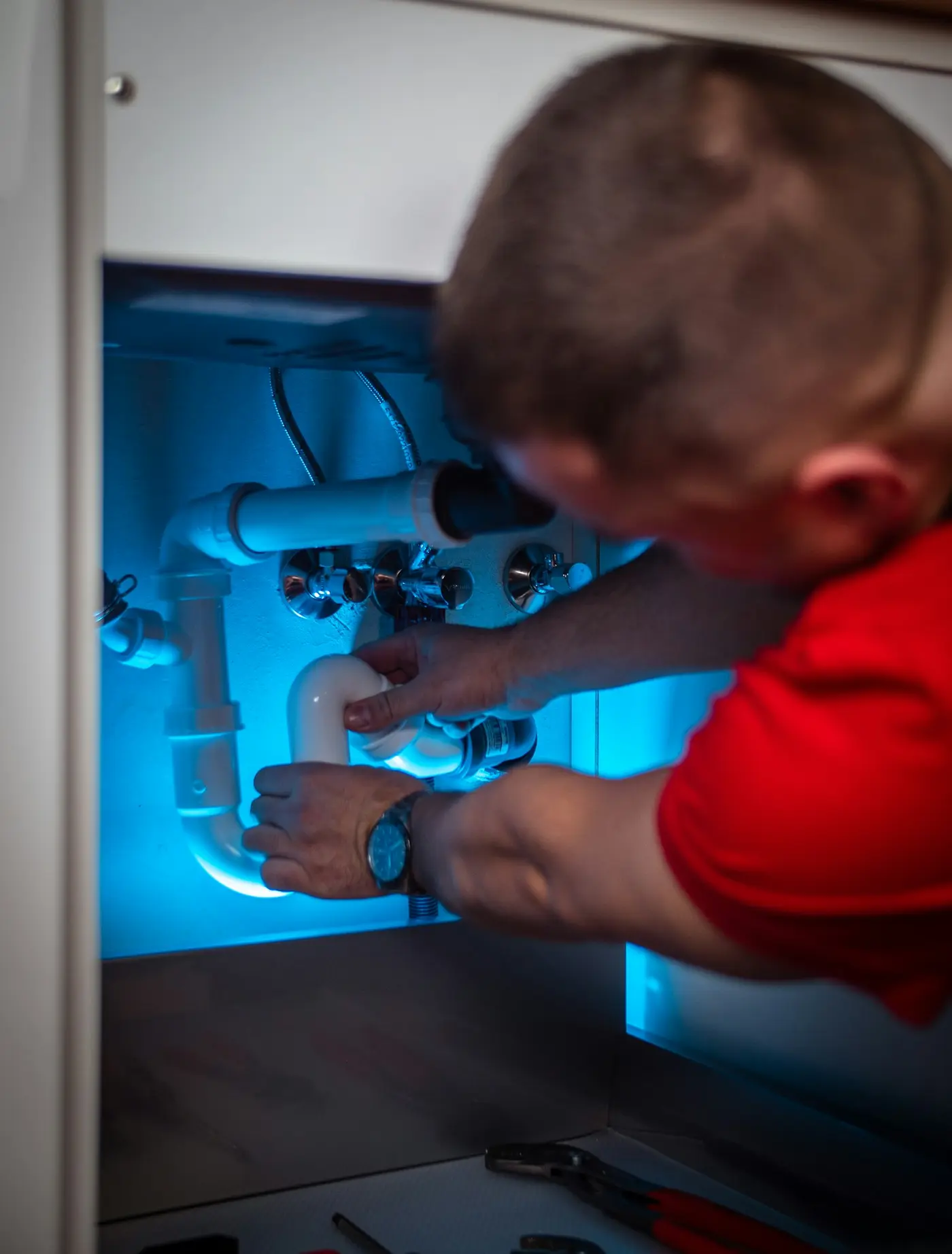 Technician connecting supply and drain lines inside a kitchen cabinet opening