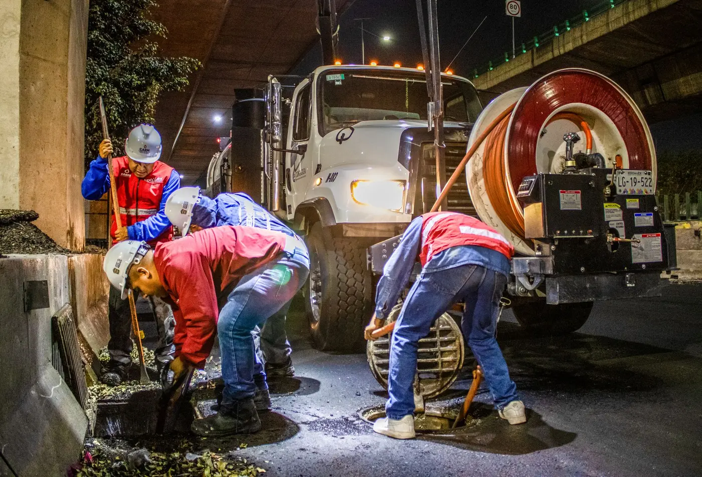 Crew clearing a blocked drainage line at night with truck-mounted equipment