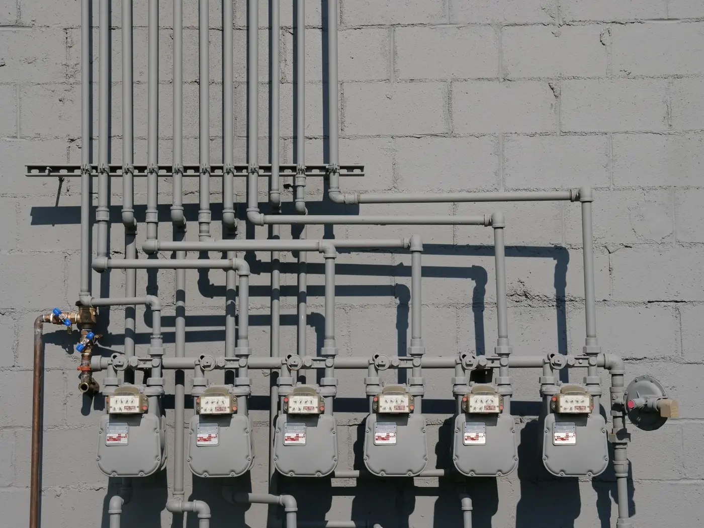 A row of gas meters and supply piping fixed to a concrete wall
