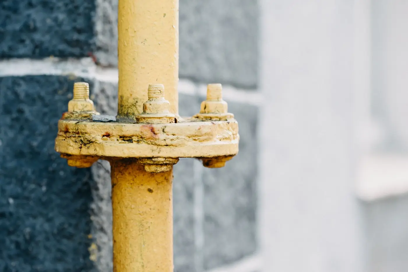 Yellow gas line pipe and its mounting hardware against a textured wall