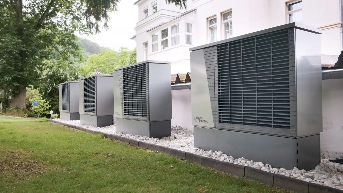 Four outdoor heat pump units lined up along a building's exterior wall