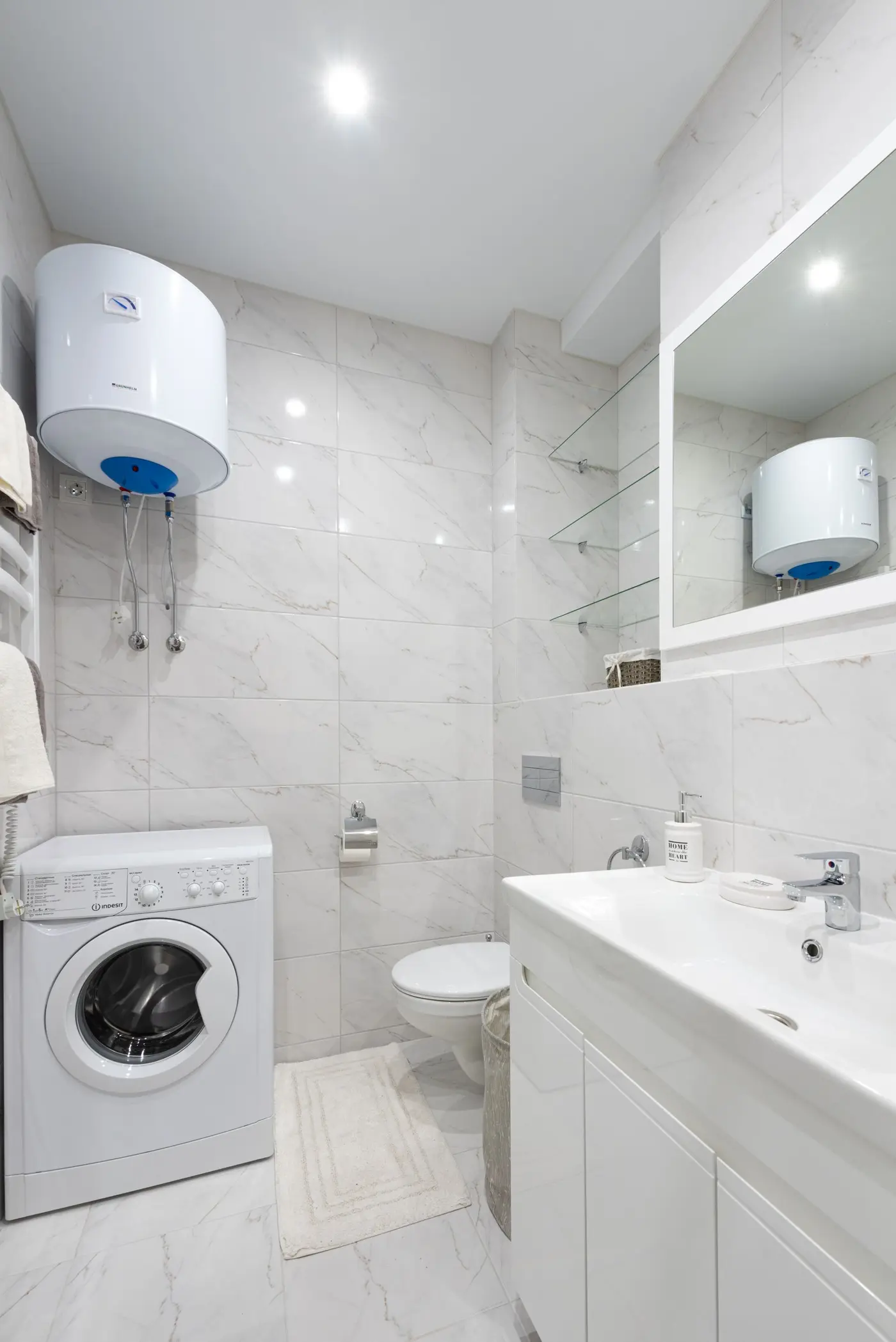 Tank water heater fitted on the wall above a front-load washing machine in a small laundry nook