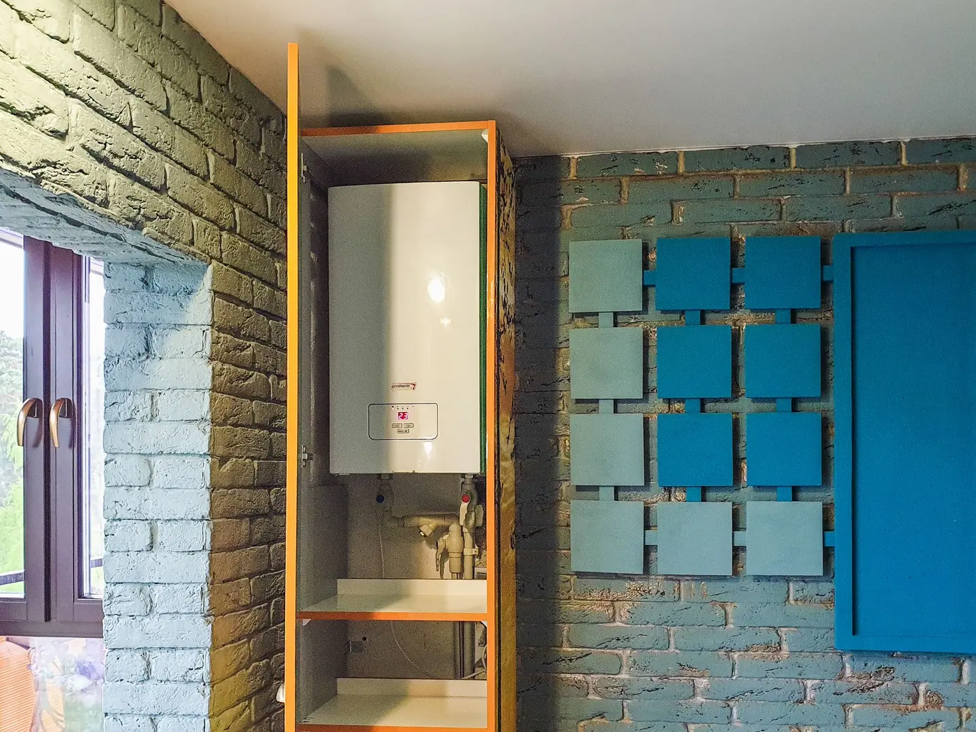 Cylindrical tank water heater mounted on the wall above a shelving unit in a home utility nook