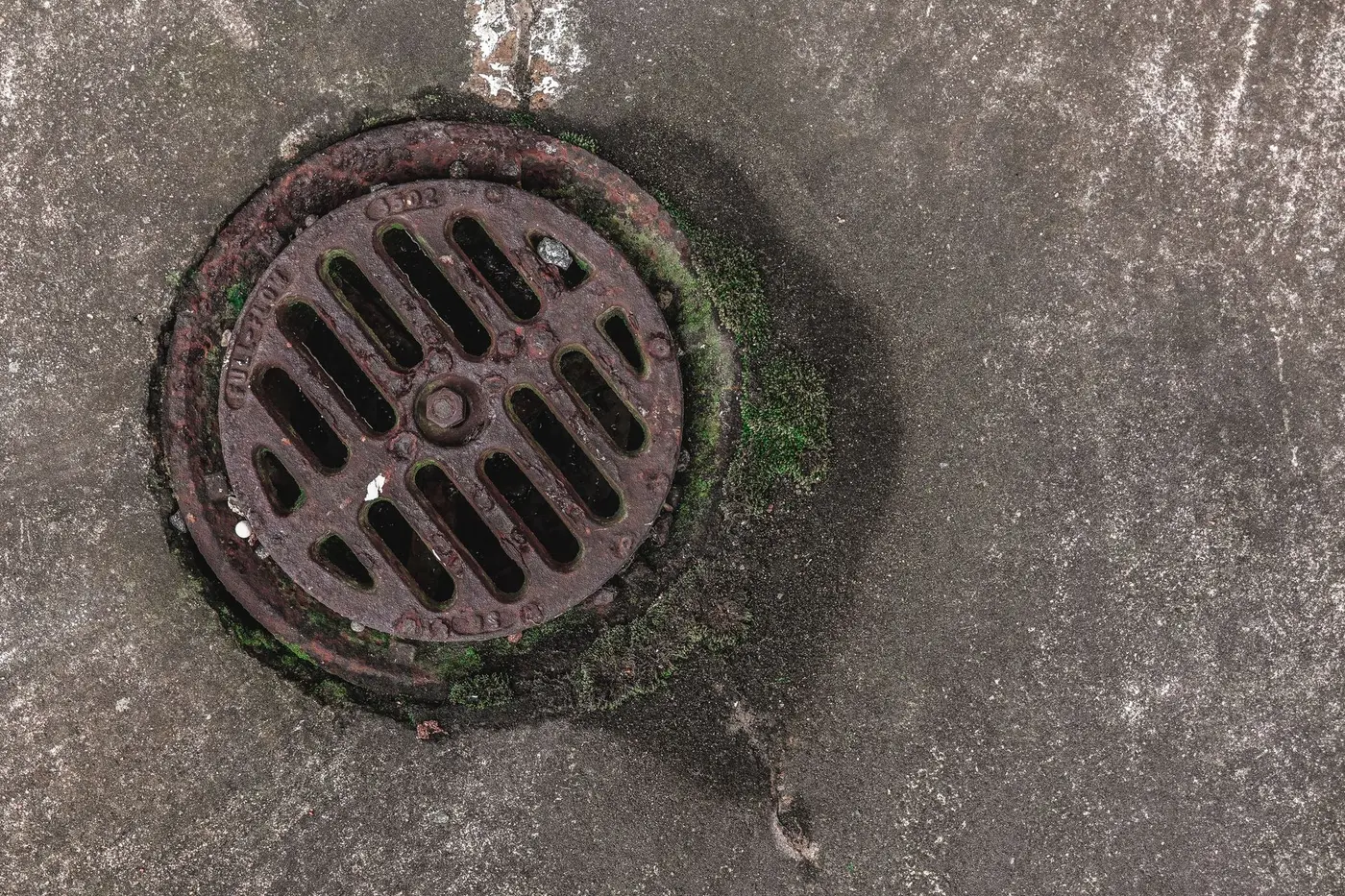 Weathered sewer cleanout cap at ground level, where a jetting hose is fed into the line