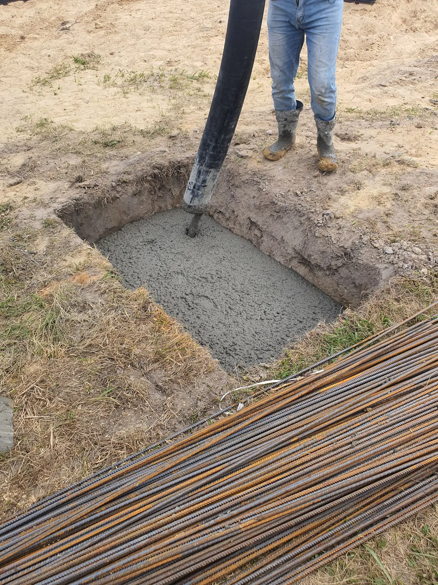 Worker standing beside an excavated foundation pit with rebar exposed