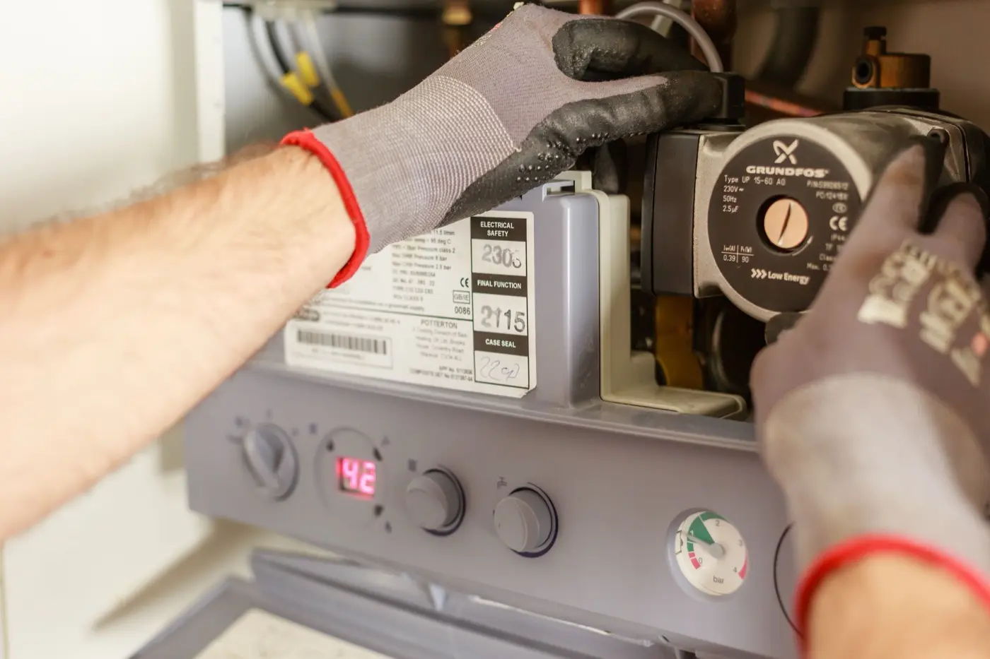 Plumber's gloved hands servicing a water heater's pump and pressure gauge before a hot water tank replacement in Abbotsford, BC