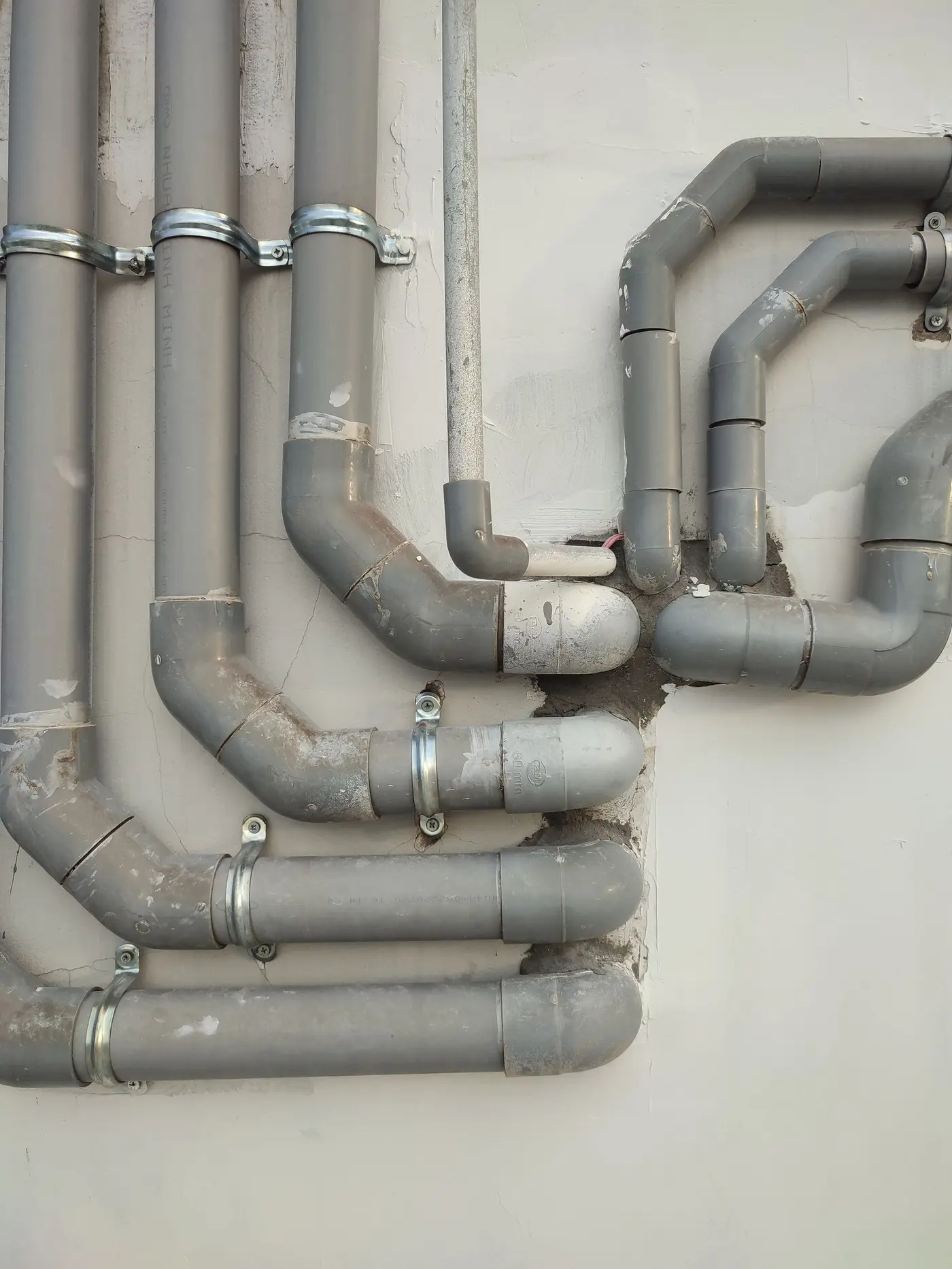 Grey plastic pipe runs and bends clamped along a wall
