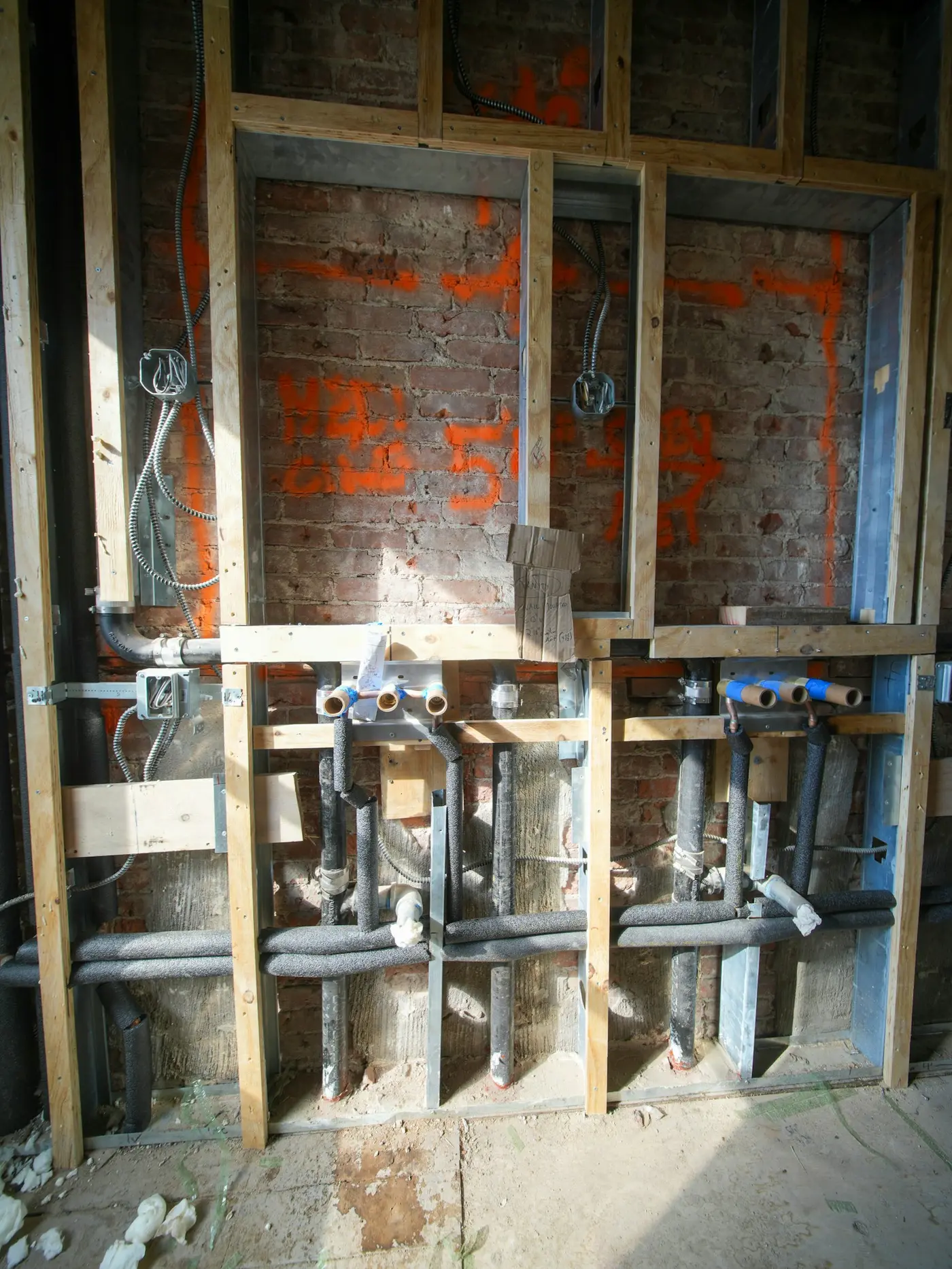 Copper pipe stub-outs and wiring exposed in a brick wall during a whole-house renovation