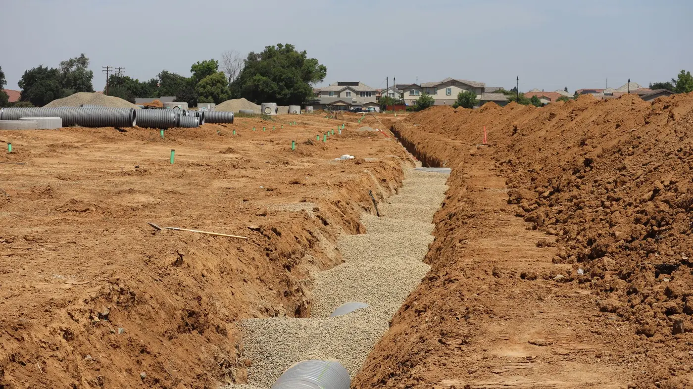 Open trench and staged sewer pipe running across a residential construction site