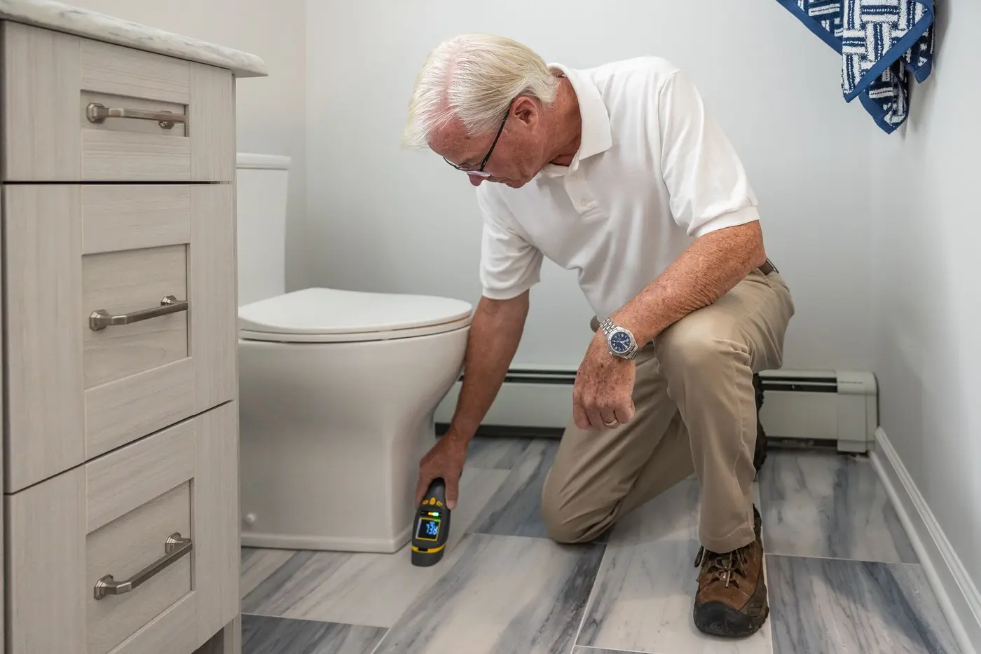 Technician kneeling to check the base and floor connection of a toilet
